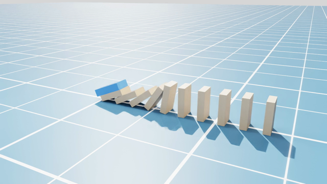 Ray-traced render: a blue starter slab tipping a row of parcel boxes mid-cascade on a pale gridded floor